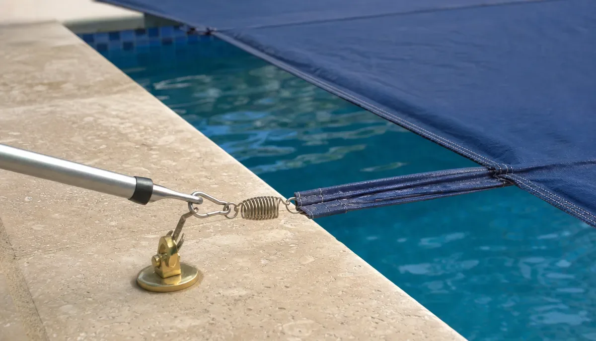 A cover spring hooked to a brass deck anchor at the edge of a pool