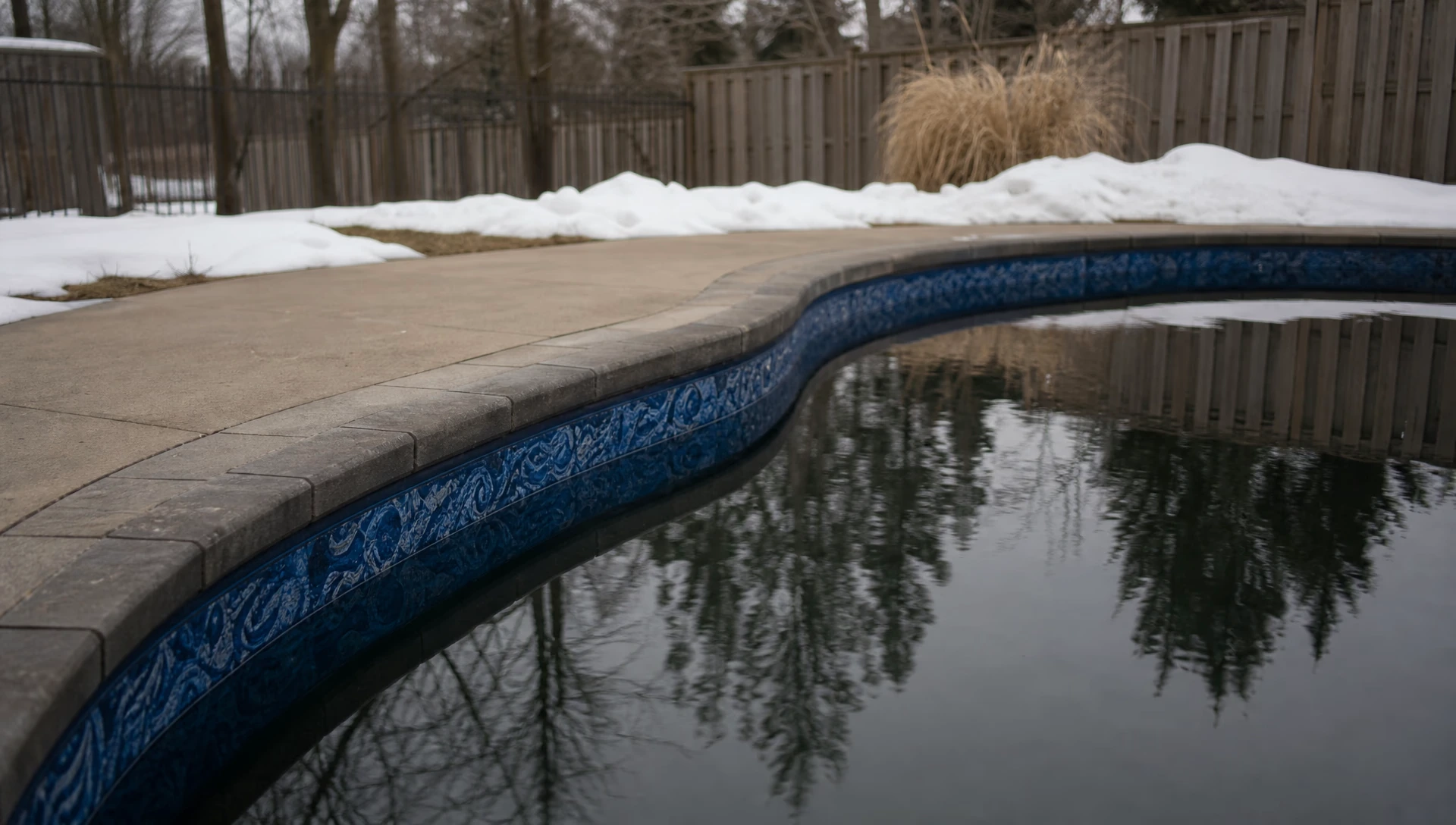 An in-ground vinyl pool in winter with the liner's waterline band visible above dark still water