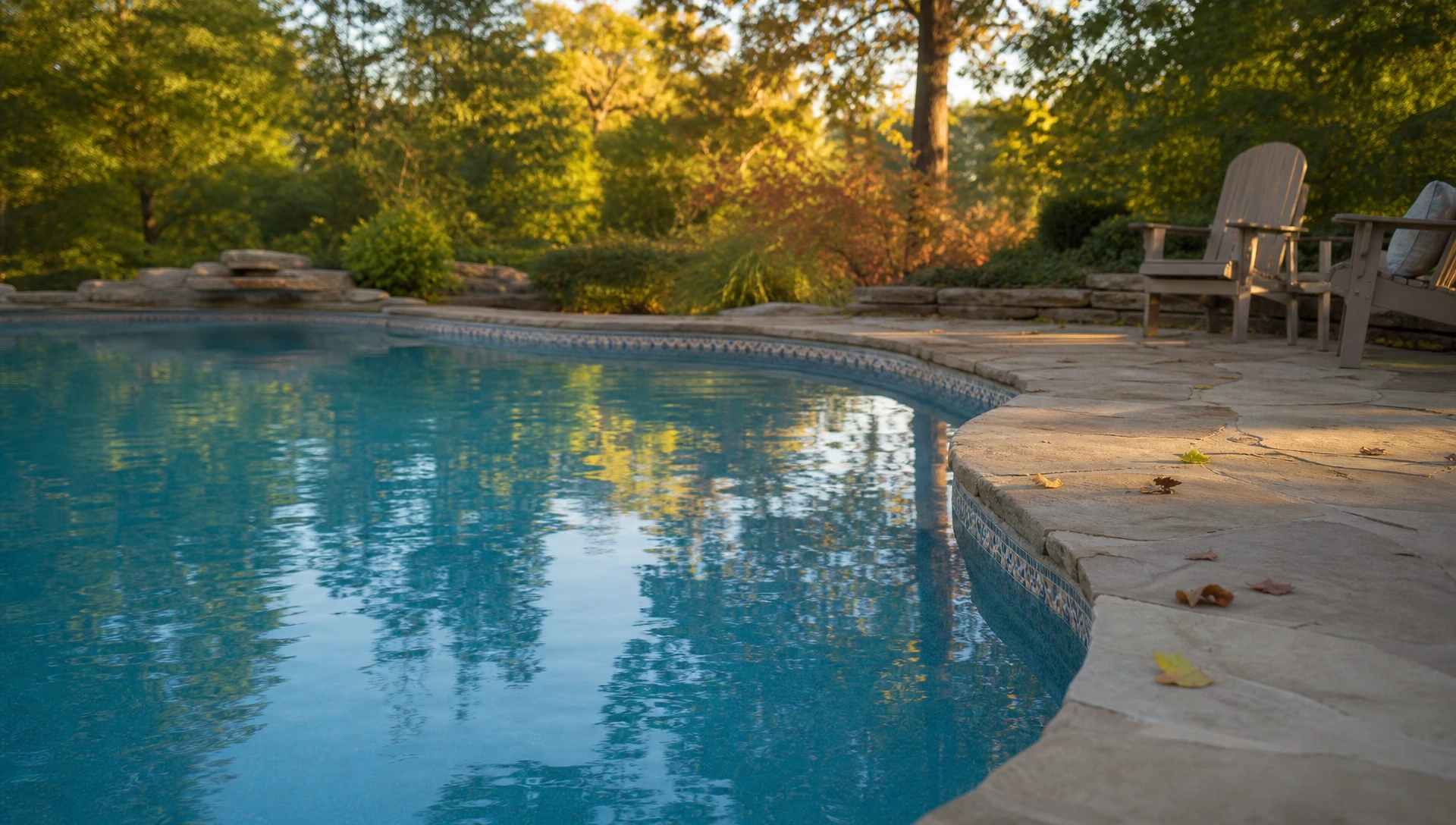 An in-ground pool still open in late September with clear water, low warm light and the first fallen leaves on the deck
