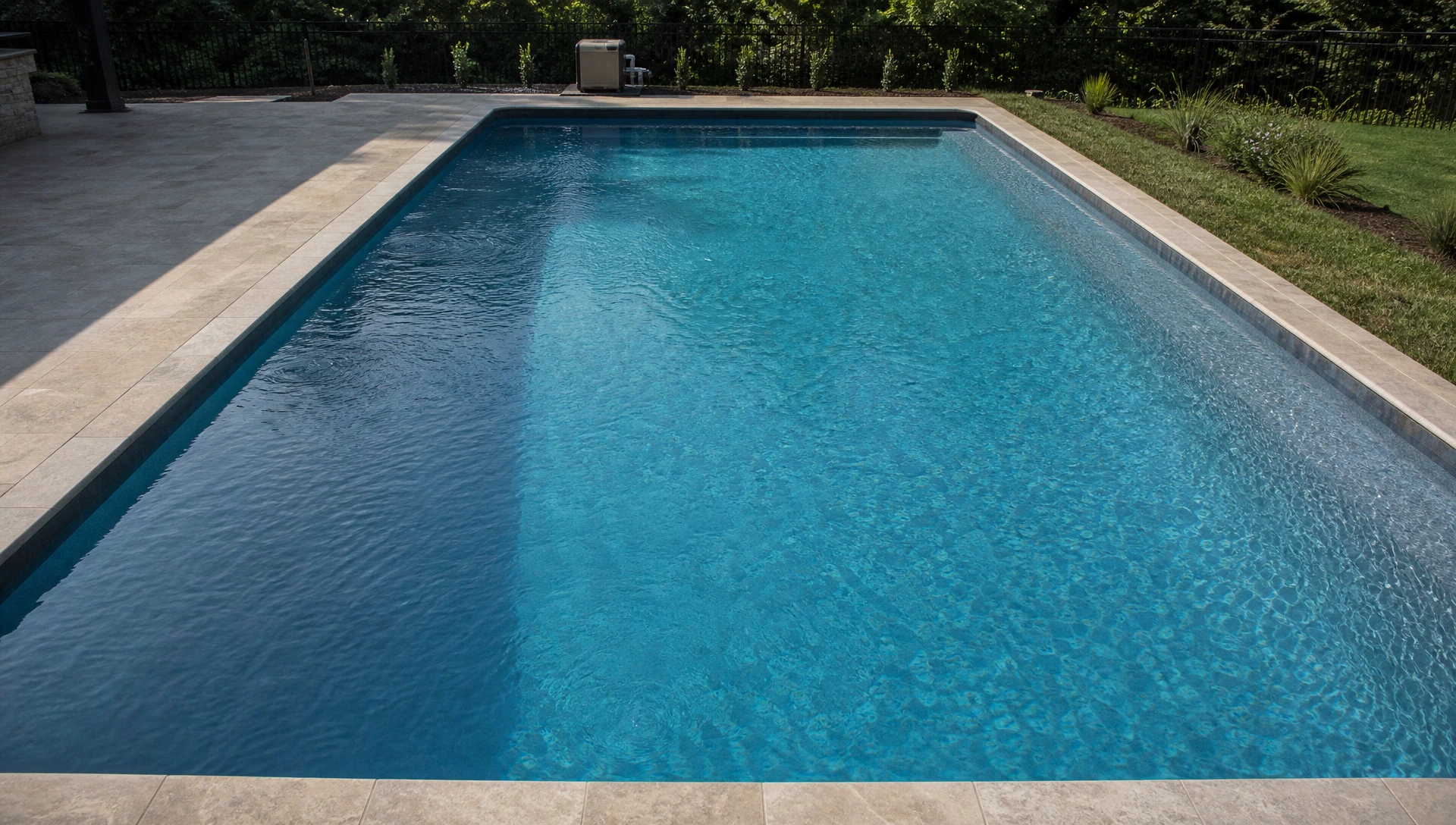 A wide in-ground pool seen from a raised viewpoint so the whole water surface fills the frame, a heater small on the pad at one end