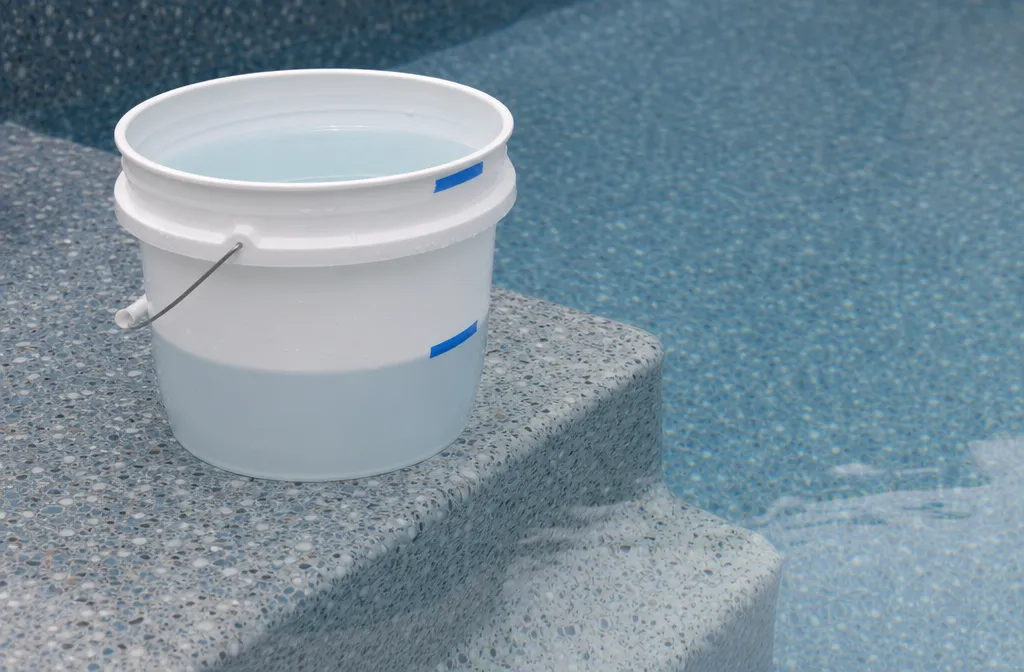 A bucket standing on the top step of an in-ground pool with its inside and outside water levels marked in tape