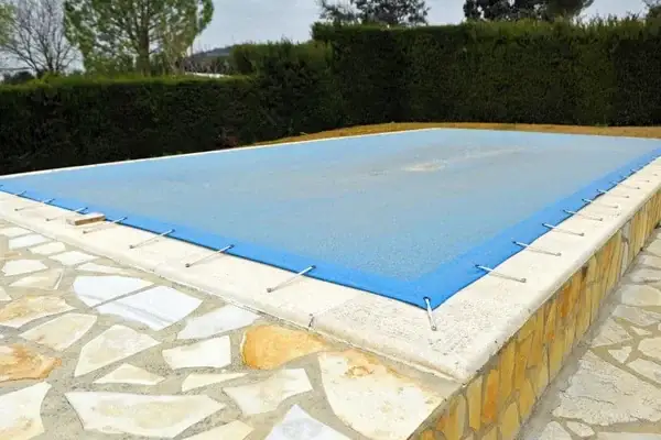 An in-ground pool closed and covered for a Northeast Ohio winter, bare trees behind