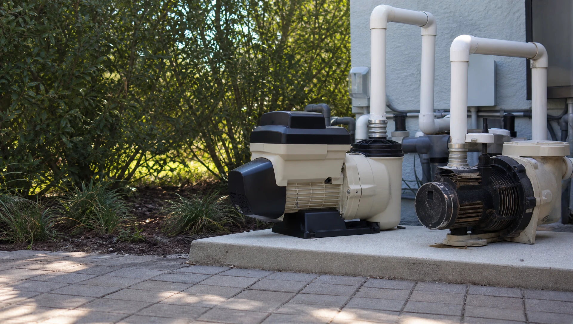 A variable-speed pool pump on a pad beside an older single-speed pump for comparison